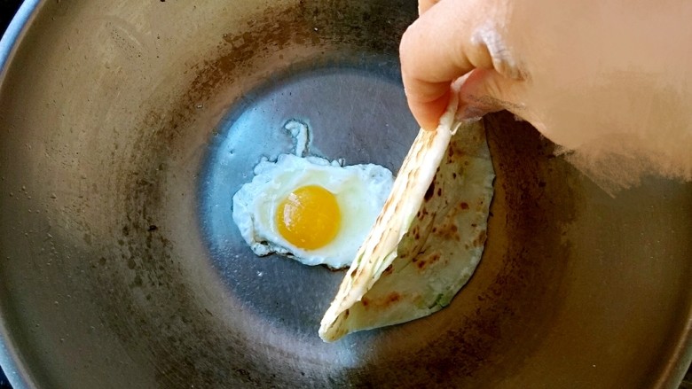 烫面鸡蛋饼,把饼盖上去。然后用锅铲用力压饼(主要是把鸡蛋黄压出来)。大约1分钟左右翻面。