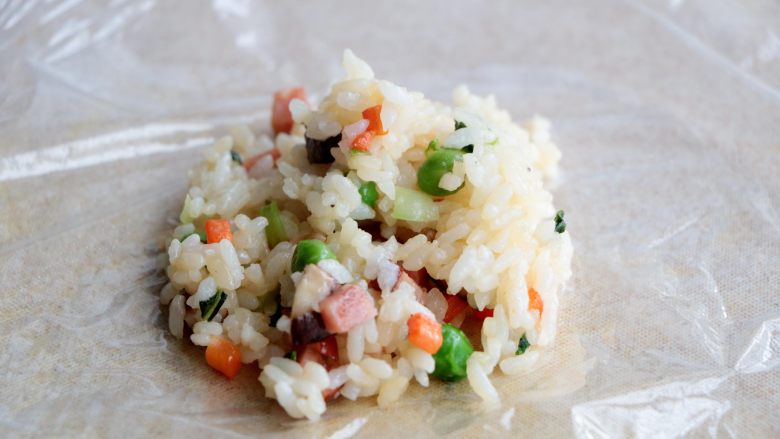 杂蔬丸子饭团,砧板上铺上一层保鲜膜,放入一勺炒好的米饭;