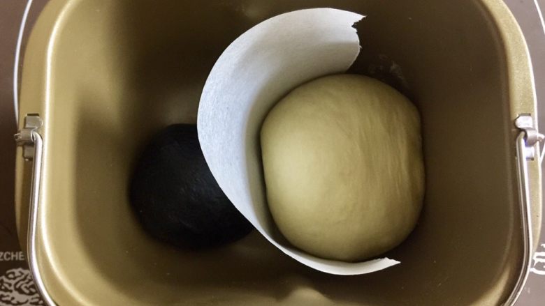 奶牛纹吐司(淡奶油版),把两个面团中间隔上一张烘焙纸,避免混色,放入面包桶,盖上保鲜膜放在温暖处进行基础发酵。参考温度28°,时间约一个小时。