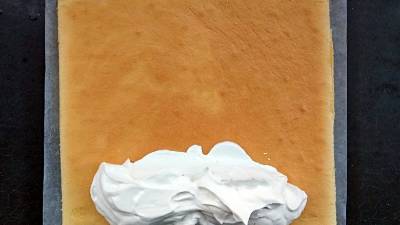 毛巾面蛋糕卷,把奶油都堆在要卷的这边,尾部稍微涂一点就ok。卷的时候需要借助擀面棍,而且也需要一张够长的油纸来辅助卷。
