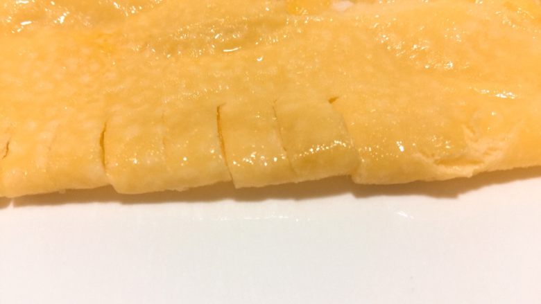 营养爱心便当🍱,鸡蛋放入平底锅,煎薄饼。取出对折,切5厘米宽等距离刀口