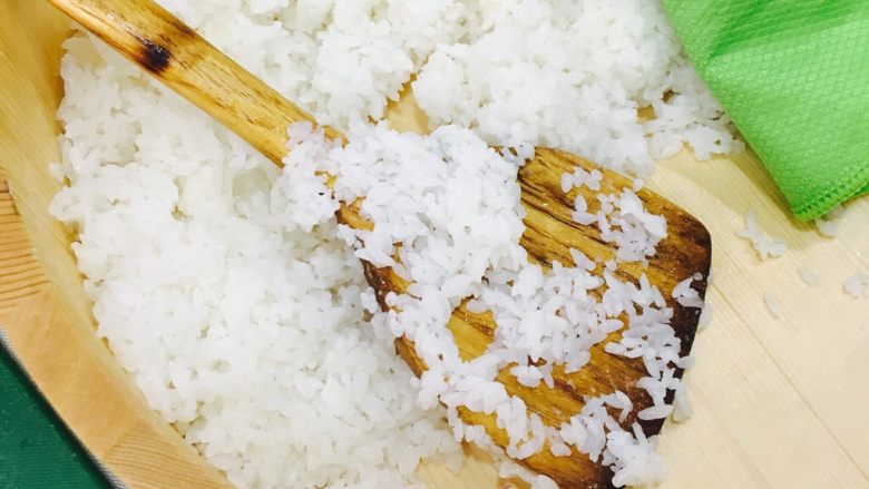 自制手握牡丹虾寿司,米饭出锅后放入木盆中,浇入1/3寿司醋,用木勺翻拌入米饭中,用屉布盖上静置10分钟