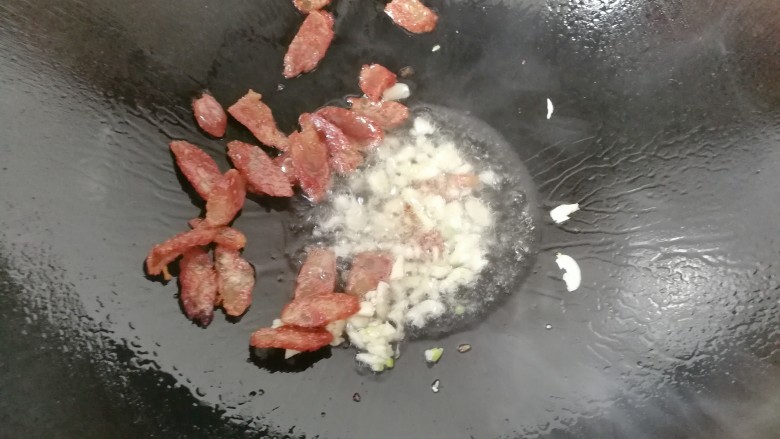 腊肠炒泥蒿,锅中入适量油,先下蒜煸香,再下腊肠煸香;