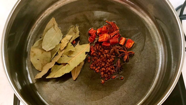 鹌鹑蛋烧排骨,炒锅烧热后放入大豆色拉油,烧热后加入花椒粒,香叶,桂皮,八角和干红辣椒翻炒1分钟