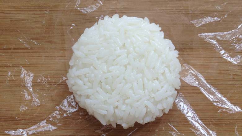 米饭汉堡,将煮好的米饭,取一小团放在保鲜膜中,用手捏紧后,再按压成饼状,大小与炸好的肉饼差不多,这样做出两个