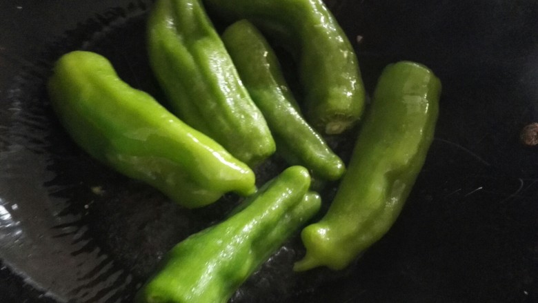 猪油渣炒辣椒豆豉,锅中放入洗净的辣椒,用中小火煎至表面起皱。