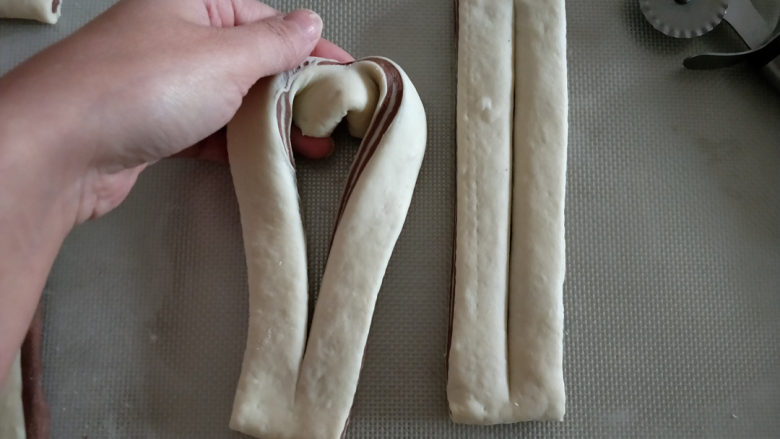 可可椰蓉卷--钟爱可可味,取一份,用轮刀在面片的中心切一刀,切透但两边不要切开。拿起一头翻向中心切开口。