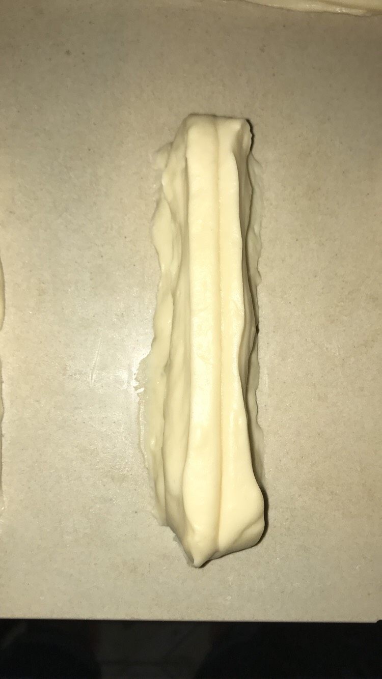 简单方便家庭自制小油条,先在面板上撒粉,也可以抹油。把面团取出,擀开,擀成长条,不要擀太宽,长就可以了。然后切成条,两条叠在一起,中间筷子一压,捏紧两头。就可以了。