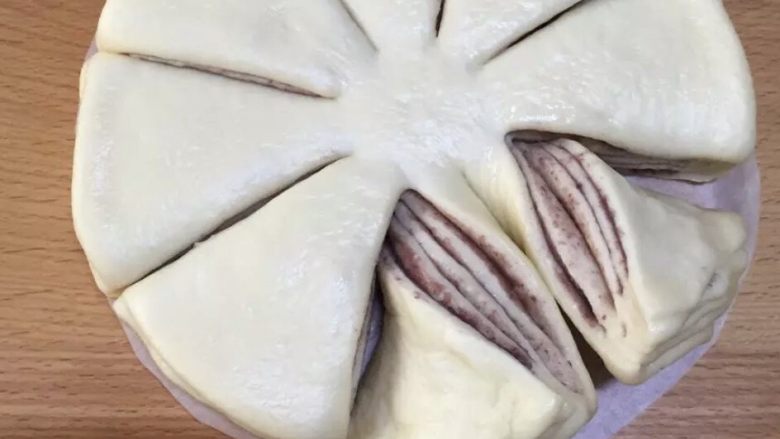 冷藏发酵黑芝麻全麦面包,铺上一层烘焙纸,在上面依次放上面团-馅料-面团-馅料-面团-馅料-面团-馅料-面团(下面一定要垫烘焙纸,不然整形后很难移动面团)。然后不切断的把面团分成8份,两片一组的扭在一起。