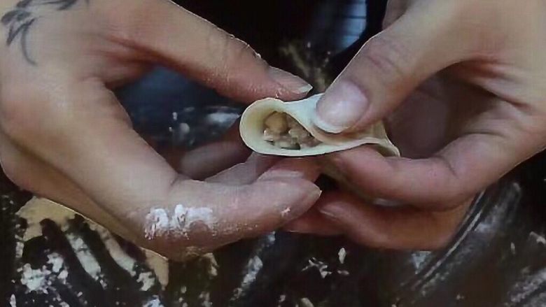 香菇猪肉饺,饺子皮平放手板心,右手食指和拇指在中心线捏一下,捏紧。。