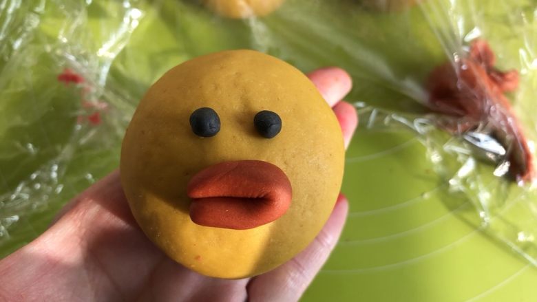 莎莉鸡豆沙包,莎莉鸡的眼睛的黑色面团是我提前做了白色面团加竹炭粉做的,嫌麻烦的话可以直接用食用黑色色素笔来画,把橘色面团取一点搓成长条,对折,粘在莎莉鸡的脸上