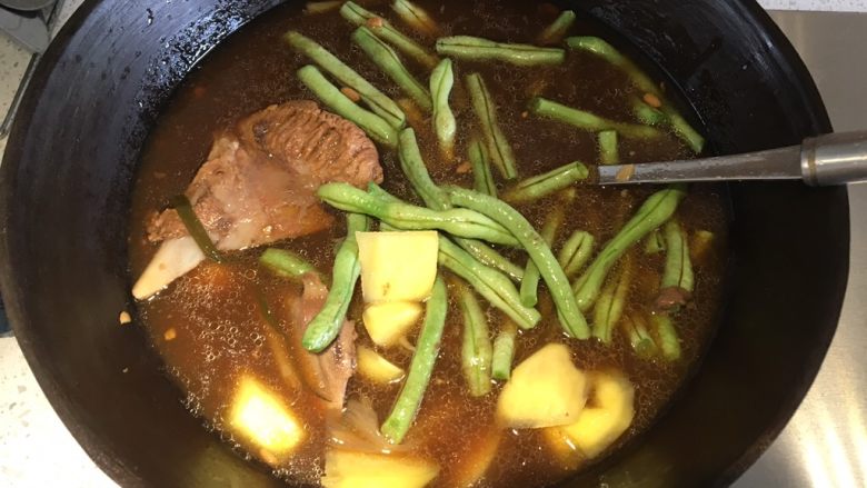 东北·乱炖,用大铁锅盛出骨头汤和一块带肉比较多的骨头,煮开,加入豆角和土豆,盖上盖子先炖熟豆角和土豆