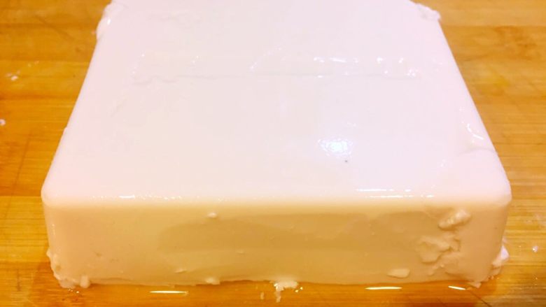 麻婆豆腐,沿着豆腐盒子四个边缘划一刀,把豆腐倒扣在砧板上,轻微抖动盒子,取出整块豆腐