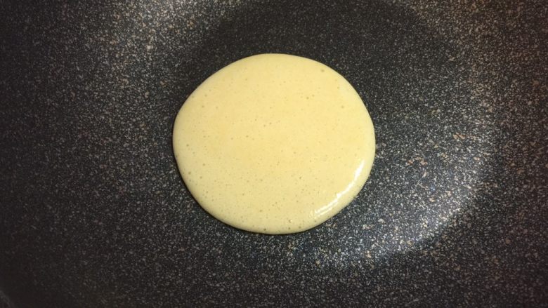奶香玉米饼,不粘锅烧热,保持小火,不放油,舀起一勺玉米面糊,从约30厘米处低落,自然形成圆形。每舀一勺的量要相同,确保每个饼的大小一致。