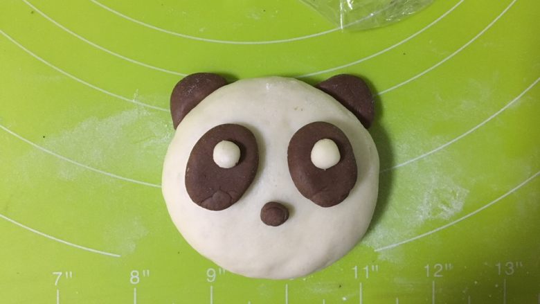 呆萌熊猫豆沙包,另取两个可可小面团,搓成椭圆形,按扁,沾一点水沾在熊猫的脸上,白面团粘在眼袋上,再取一点点可可面团作为鼻子