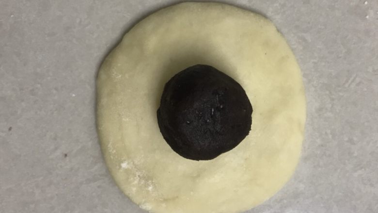 奶香豆沙小餐包,取一个面团,收口朝上用手掌拍打成中间厚边上稍薄的面皮,放上豆沙