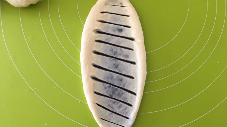 豆沙面包圈,用擀面杖擀成椭圆,用刀片斜着割10多刀,从长边开始卷起