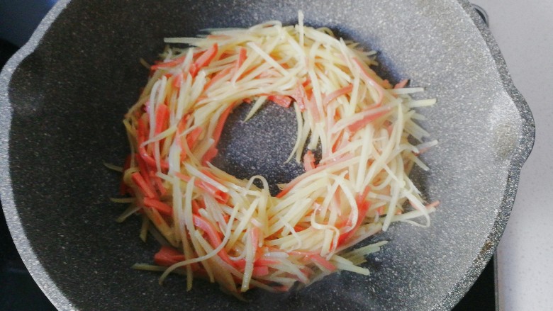 火腿土豆烘蛋,然后把火腿土豆丝用锅铲拨成一个圆圈形;