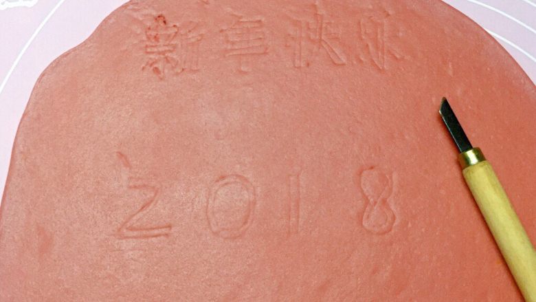 新年快乐,然后取一红色面团擀成1cm厚的面片,用美工刀轻轻地刻写出“2 0 1 8 新 年 快 乐 ”的字样。