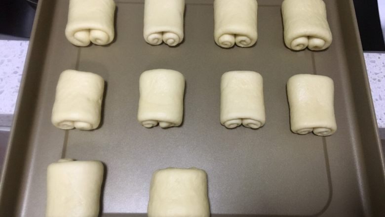 日式牛奶面包卷,卷好的面团放入烤盘,每一个面团之间要留空隙,喷壶喷上清水保湿,放入烤箱,发酵档发酵40分钟