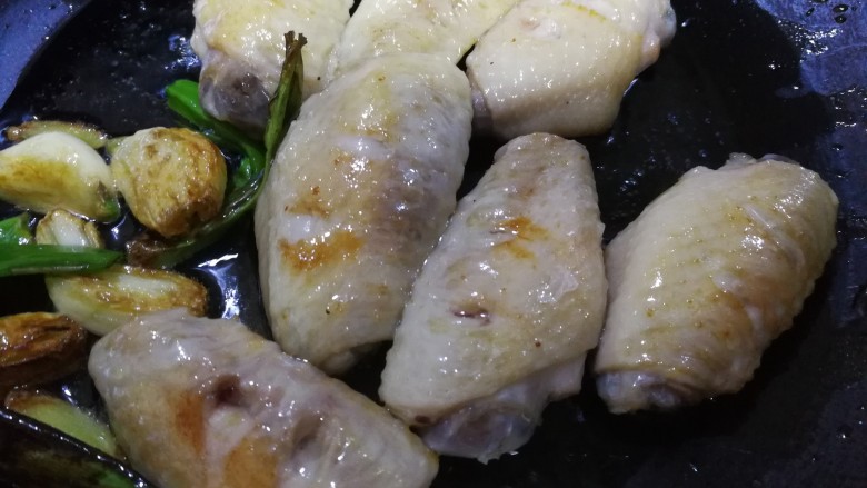 梅子(话梅)鸡翅,炒菜的铁锅烧热后倒入煎好的鸡翅,油也放一点进去,同时把刚才挑出来的葱姜蒜瓣也放进锅里