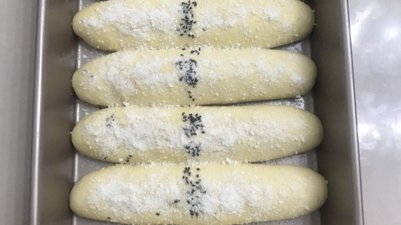 70%中种炼乳排包,送进发酵箱,里面放上一碗热水制造湿度,保持在80%左右的湿度,温度调节在34度,发酵二倍大后,表面刷上全蛋液,中间撒上黑芝麻,再撒上椰蓉装饰