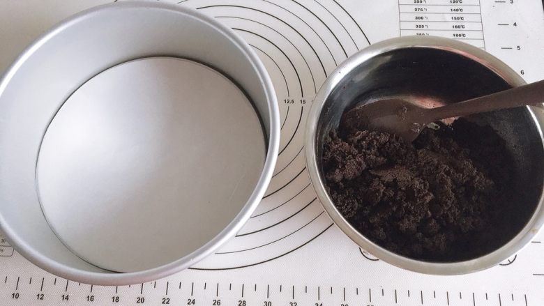 草莓装饰慕斯蛋糕,将黄油隔热水彻底软化后与饼干碎充分混合均匀,模具底部放入油纸。