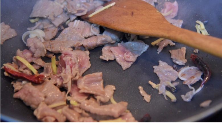 时蔬炒牛肉,翻炒肉片,变色后加葱姜,翻炒。