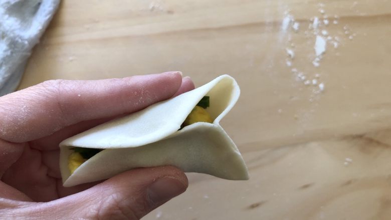 手工韭菜鸡蛋饺子,对折饺子皮,中间处捏合,然后如图所示,两边从中间推进去,捏紧,然后凸出来那一小块再从凸出处往里按压捏紧
