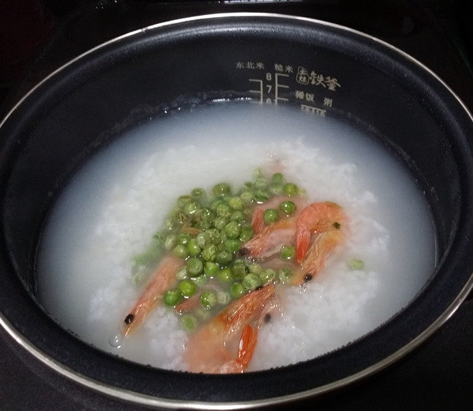 #电饭煲# 蔬菜海鲜粥,打开电饭煲,放入刚煸好豌豆大虾、用饭勺搅拌均匀加盖继续