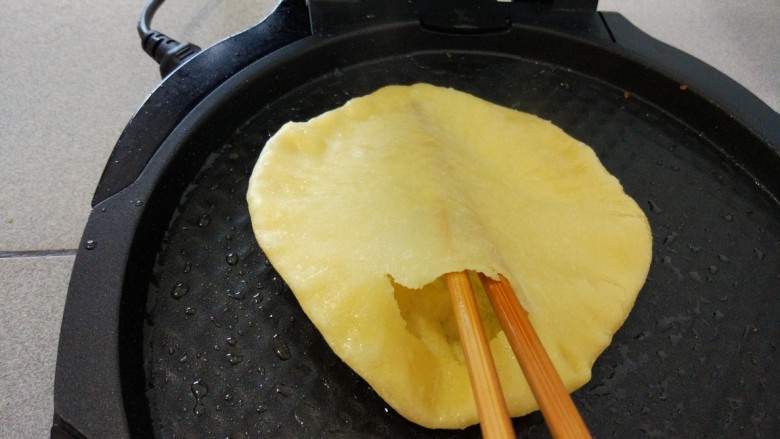 金灿灿—鸡蛋灌饼,大约两分半钟,饼皮鼓起,上下层分开,用筷子在饼胚边缘戳一个洞,让筷子穿过整个饼皮提起,灌入一颗鸡蛋,用手摇晃均匀。