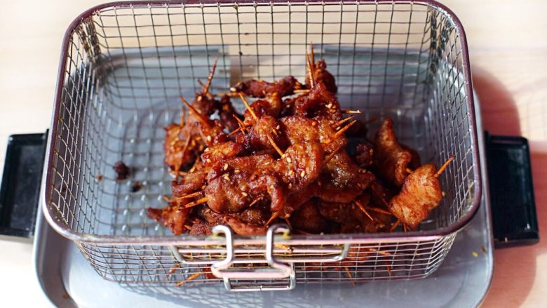 秘制牙签肉,锅内放油,烧至七成热,下入穿好的牙签肉炸至表面微微泛黄,然后捞起放沥水篮沥干油份。