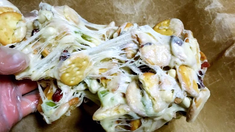 网红雪花酥,戴手套趁热将材料拉扯开,再对折,将果干跟饼干充分的拌均匀