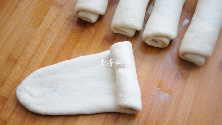 老字号甜咸味椒盐油酥金丝饼,把面团压扁,用擀面杖从中间向两头擀开成椭圆状,再从一头卷起来,卷到另外一头压紧。
