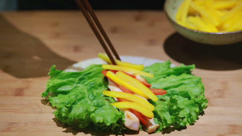 饭爷特制鸡肉卷,将饼皮平放,长叶生菜放置上面,涂上【饭爷】松露油杏鲍菇辣酱后,将鸡肉和彩椒依次摆放在生菜中间。