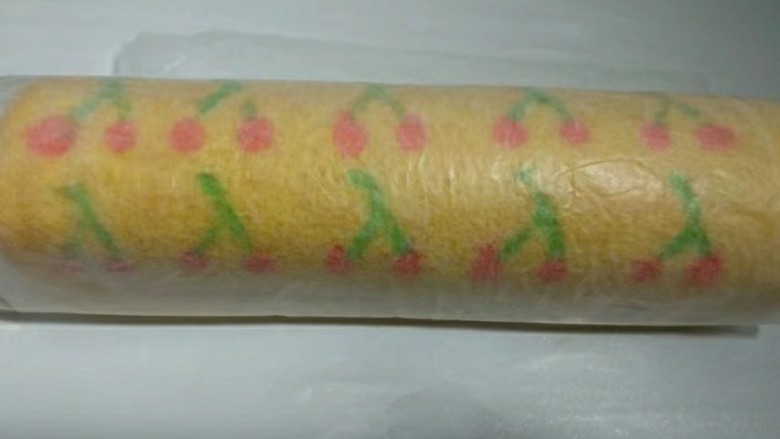 手绘樱桃南瓜豆浆蛋糕卷,将烤盘取出震一下,倒扣在烤网上。趁热小心撕开油纸,再重新盖上一张新的油纸。倒扣过来,烤黄的那面朝上,把蛋糕卷起来,尽量卷紧一些。定型5分钟就可以切开享用了。