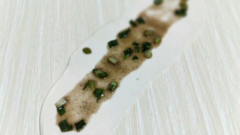 烫面椒盐葱花酥饼,取一块面团,用擀面杖擀长舌状,均匀涂抹上椒盐。