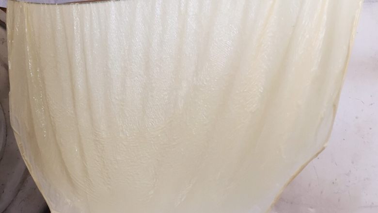 纯手工豆腐皮,如图:用双手将龙须拉起,一张白色的豆腐皮就从锅中捞起来了。