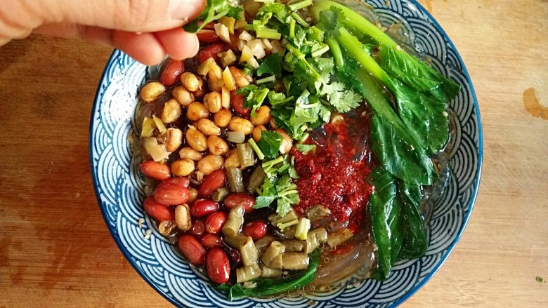 酸辣粉,把焯熟的油菜放在表面,在粉上撒炸酥酥的花生米、黄豆、香菜、酸豆角、榨菜碎,再浇上一勺油泼辣子,一道软韧劲道的美味酸辣粉制作完成。