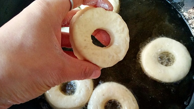 甜甜圈,锅中宽油，烧至七八成热（温度在180°C左右），将二次醒发后的甜甜圈饼坯下油锅。