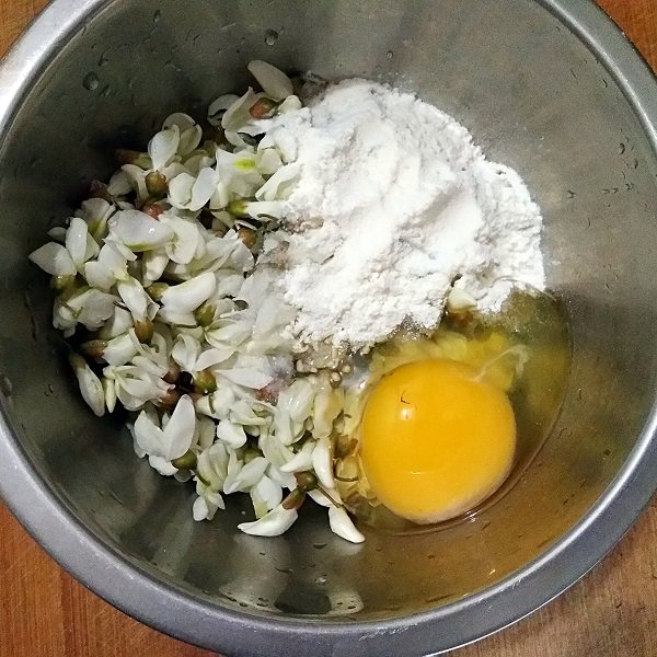 做饼+槐花塌子,将洗净的槐花沥水后放进容器,打入1个鸡蛋,加入适量面粉和少量的盐。