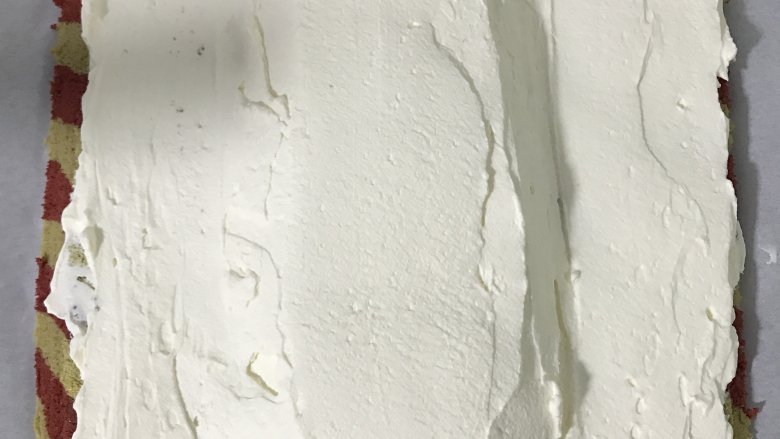 双色蛋糕卷,蛋糕卷两边斜切,抹上淡奶油,中间厚两边薄,将两边油纸向中间拎起,在用手辅助整成O型卷。包好油纸放入冰箱冷藏半个小时以上定型。