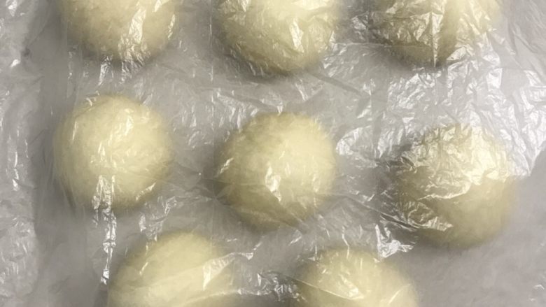 椰蓉花朵面包,取一个面团光滑面在上,分割下来的小块压里面滚圆盖上保鲜膜松弛15分钟。