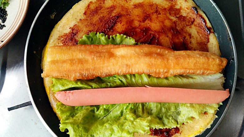 做饼+煎饼果子,放入油条(薄脆果篦儿),生菜和<a style='color:red;display:inline-block;' href='/shicai/ 437'>火腿肠</a>。我家的天津老佛爷说:“在煎饼果子里放生菜和<a style='color:red;display:inline-block;' href='/shicai/ 437'>火腿肠</a>的都是邪教,正宗的天津煎饼果子只放油条或果篦儿。”我说:“这是我大山东的改良版,这才叫营养又接地气!哈哈哈!”