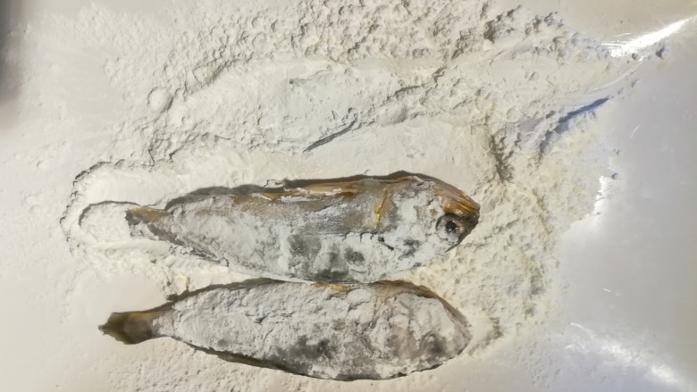 家常小黄鱼贴饼子,我们来把鱼处理好,沥干水分,找一个大盘子,里面放上淀粉,把鱼两面沾上淀粉。