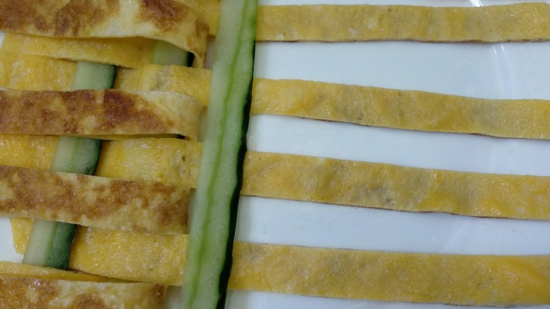菠萝咖喱饭,大盘子上抹少许植物油,将鸡蛋条和黄瓜条用编花篮的方法编织在一起,如图。