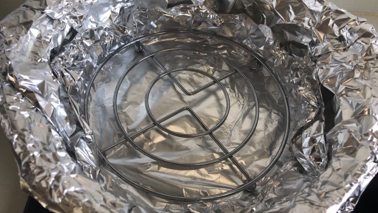 砂锅烤红薯,用两张锡纸交替把砂锅内部包裹起来,放入一个支架。(裹锡纸是因为红薯在高温烘烤下会溢出糖浆,留在砂锅底部会形成难以清洗的顽渍。)