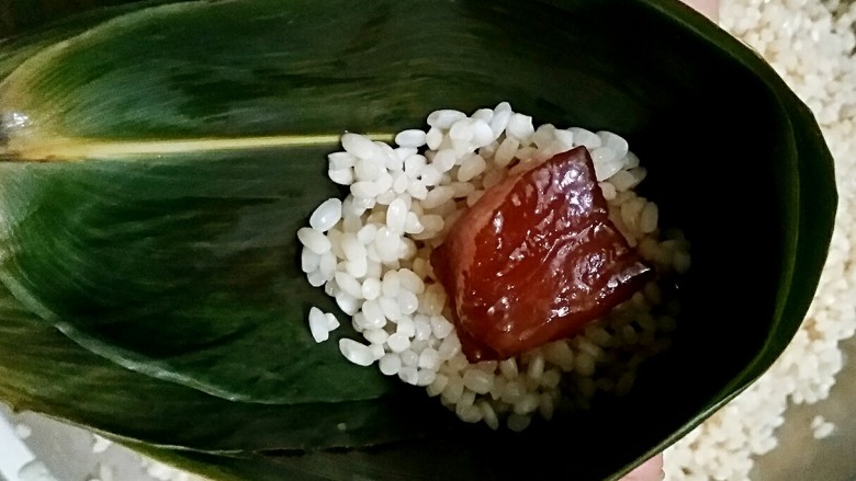 鲜肉粽子,取两张泡好的粽叶,毛面相贴(用手能摸出来,一面光滑,一面微涩即为毛面),在叶尖三分之二的地方卷成60度左右的倒漏斗型,在卷好的漏斗内加三分之一的糯米,然后加肉。