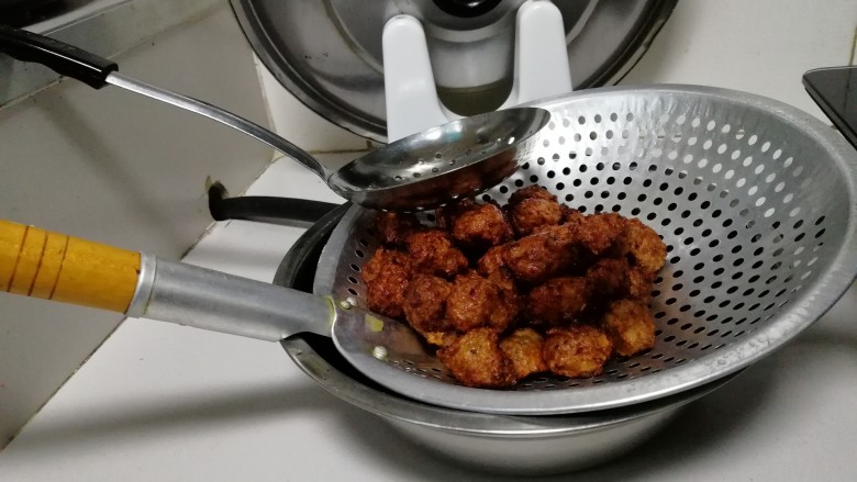 秘制油炸肉丸,放置在另外一个大漏勺里,底下放个碗沥油