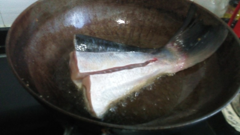 红烧鱼划水,热锅的表面用生姜涂抹一下,热锅放油润锅,关火冷却,这样防止糊锅。把鱼尾上的杂料去除干净,用厨房纸把水分沾干,锅中再次放油,五成热下入鱼尾,中火煎制定型。
